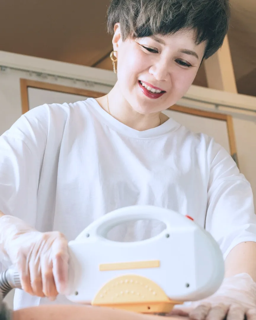 サロンのオーナーが、施術用のハンドピースを手に笑顔で話しているところ。